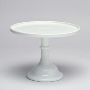 A white ceramic cake stand with a wide, flat top and sturdy pedestal base.