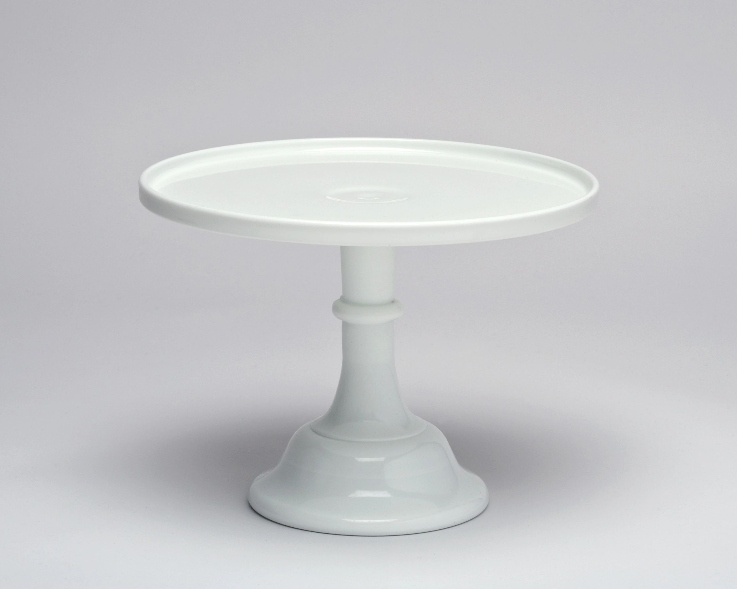 A white ceramic cake stand with a wide, flat top and sturdy pedestal base.