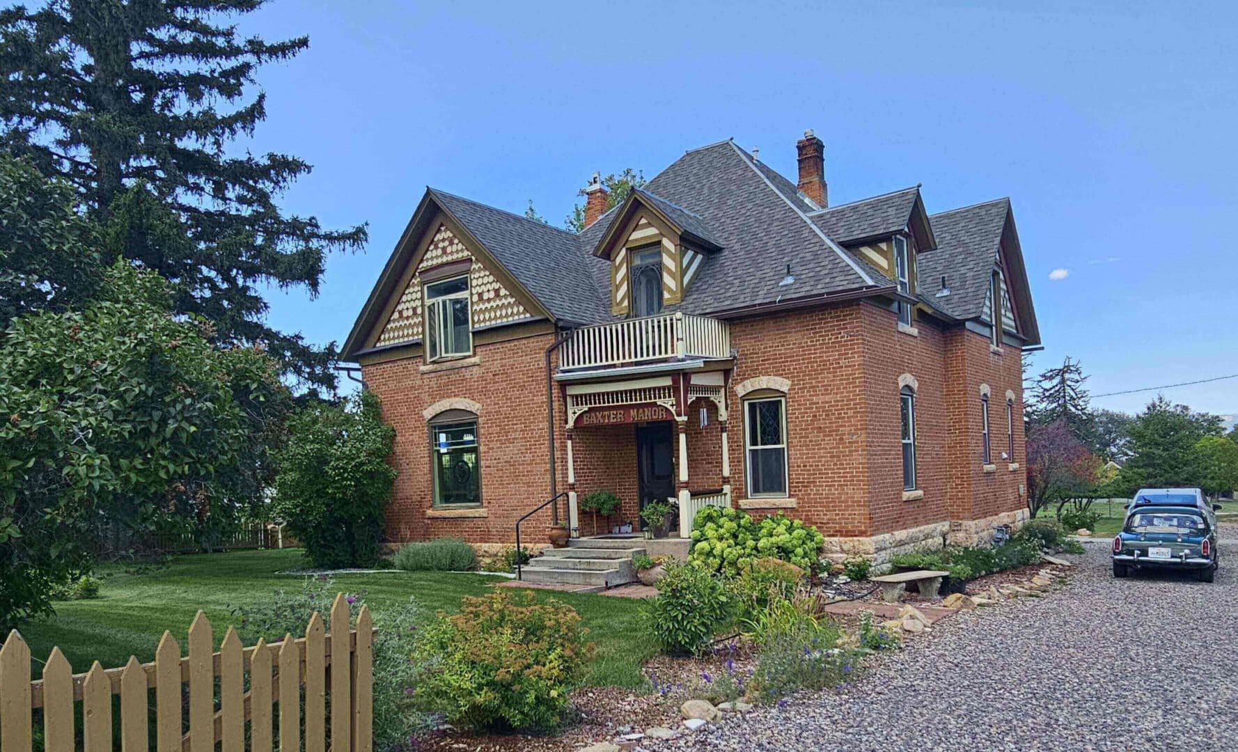 A large brick house with a steep roof and front porch in a rural setting.